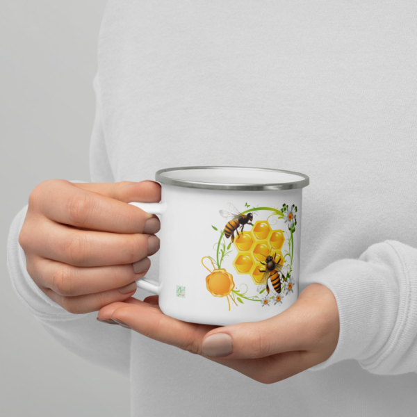 Taza esmaltada abejas en manos vista frontal Taza esmaltada abejas, sostenida en las manos, vista frontal