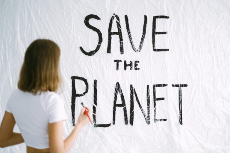Back view of woman painting 'Save the Planet' message on wall, promoting environmental awareness.